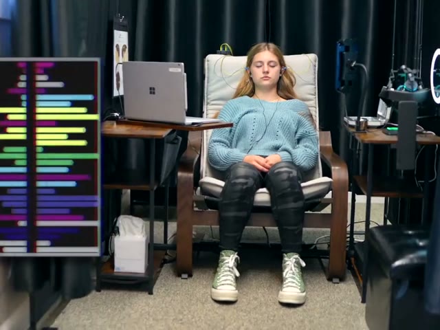 A client relaxing in a session chair beside a live readout of her brainwaves